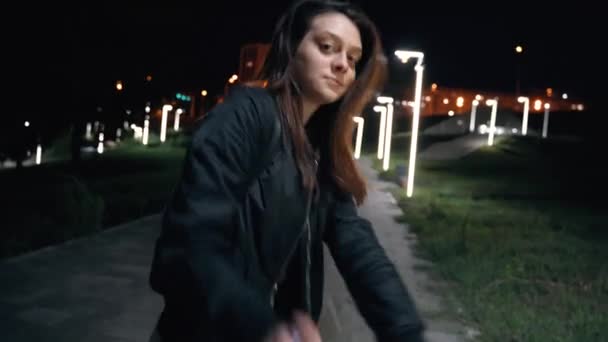 En ung ambitiös kvinna i utsvängda byxor glatt dansar i en nattpark — Stockvideo