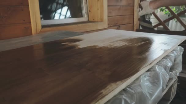 Mannelijke hand in een handschoen bedekt een houten tafelblad met een borstel — Stockvideo