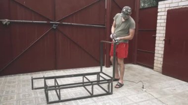 İş üniformalı ve eldivenli genç bir adam metal bir çerçeveyi bir yağ çözücüyle siliyor.