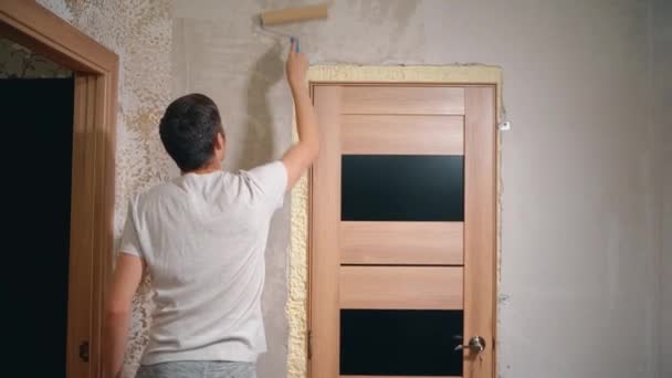 Ein Mann hält eine Walze in der Hand und überklebt die Spachtelwand mit Klebstoff — Stockvideo