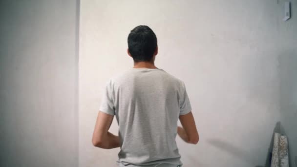 Giovane uomo cammina fino a parete intonacata bianca — Video Stock