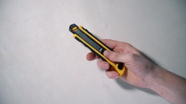 Male hand holds a yellow clerical knife and opens it on a white background