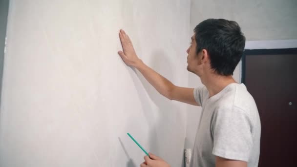 Young man walks up to a white plastered wall and checks for waves — Stock Video