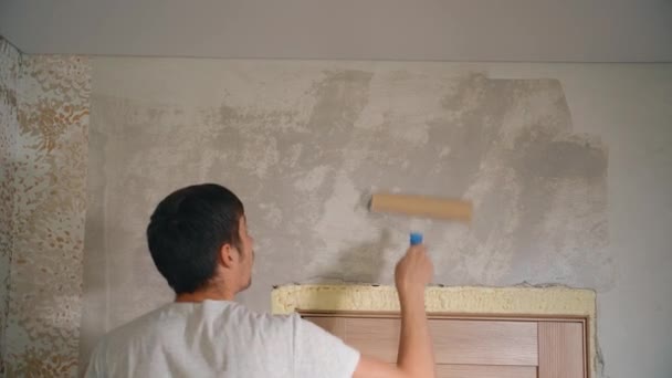 Un uomo tiene un rullo tra le mani e copre la parete di stucco con colla — Video Stock