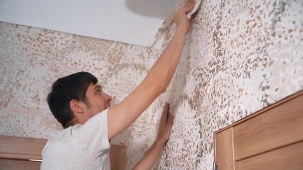 新しいアパートで男は注意深くきれいに壁紙を接着します。 — ストック動画