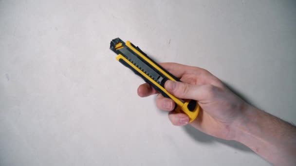 La mano masculina sostiene un cuchillo clerical amarillo y lo abre sobre un fondo blanco — Vídeos de Stock