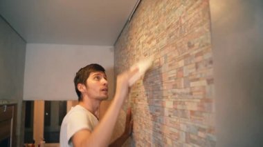 A married couple makes repairs in their house, neatly gluing wallpaper