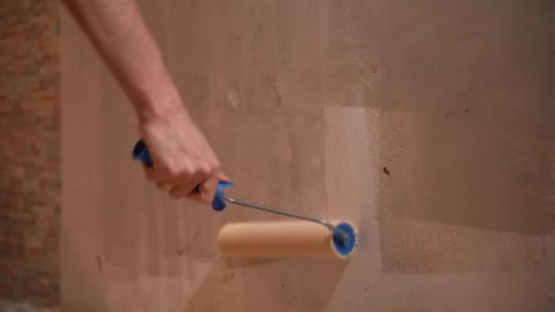Ein Mann hält eine Walze in der Hand und überklebt die Spachtelwand mit Klebstoff — Stockvideo