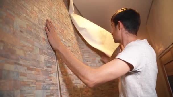 Чоловік робить ремонт в своєму будинку, акуратно приклеюючи шпалери — стокове відео