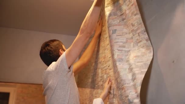 Молода сім'я робить ремонт в будинку, склеюючи шпалери — стокове відео