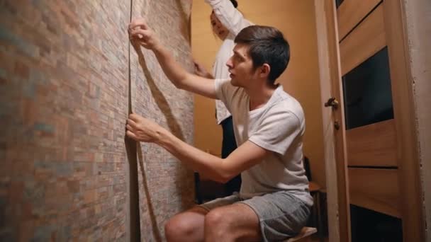 Супружеская пара делает ремонт в своем доме, аккуратно склеивая обои — стоковое видео