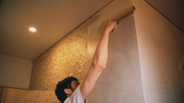 Ein Mann hält einen Pinsel in der Hand und überklebt die Spachtelwand mit Klebstoff — Stockvideo