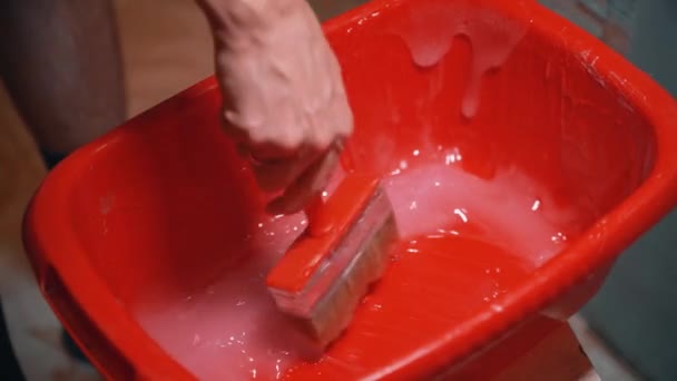 A mans hand holds a brush and soaks it in glue for gluing wallpaper — Stok video
