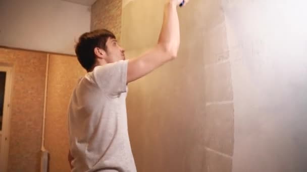 A man holds a roller in his hands and covers the putty wall with glue — Stock Footage A man holds a roller in his hands and covers the putty wall with glue Stock Footage