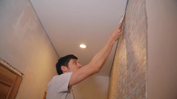 Un hombre pega cuidadosamente el papel pintado en un apartamento nuevo — Vídeos de Stock