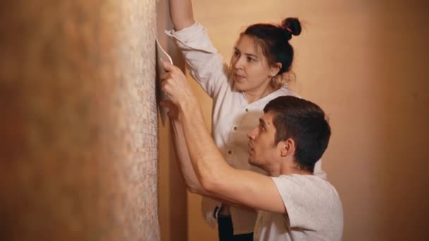 Feliz familia joven haciendo renovaciones en su nuevo apartamento, pegando papel pintado — Vídeos de Stock