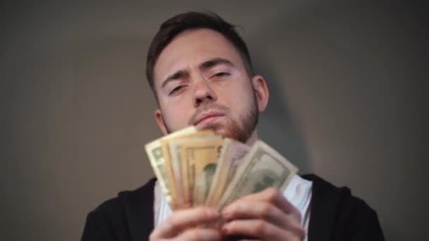 Young man waving a fan of dollar bills in front of his face — Stock Video