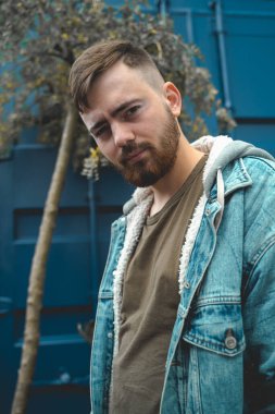 Kot ceketli yakışıklı sakallı adam arka planda duruyor.