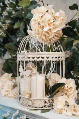 Yapay çiçekler ve mumlarla dekoratif kafes, hassas kompozisyon.
