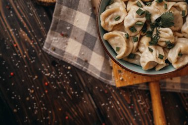 Derin bir tabakta kaynamış hamur köfteleri taze soğanlar, mutfak aletleri, ahşap kesim tahtaları serpiştirilmiş.