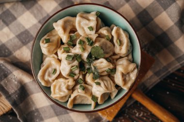 Derin bir tabakta kaynamış hamur köfteleri taze soğanlar, mutfak aletleri, ahşap kesim tahtaları serpiştirilmiş.