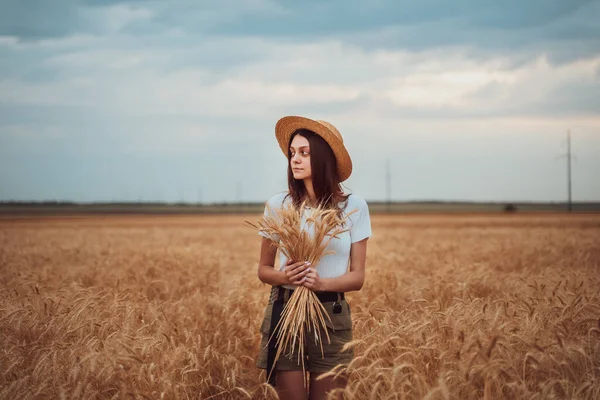 Dziewczyna w słomkowym kapeluszu stoi na polu pszenicy z bukietem — Zdjęcie stockowe