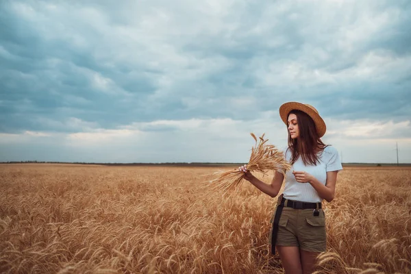 Dziewczyna w słomkowym kapeluszu stoi na polu pszenicy z bukietem — Zdjęcie stockowe