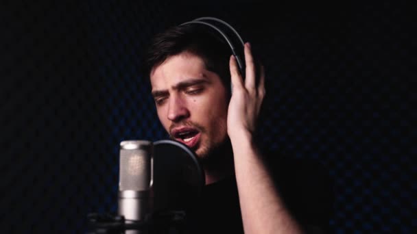 Ένας άνθρωπος με ακουστικά εκτελεί συναισθηματικά μια λυρική σύνθεση σε ένα μικρόφωνο — Αρχείο Βίντεο