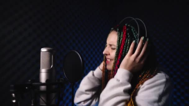 Mujer joven con el pelo de color se para en un estudio de grabación en auriculares — Vídeos de Stock
