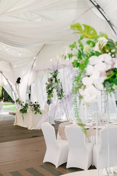 Wedding decoration of a photo zone and tables with fresh flowers, tent decor, green plants