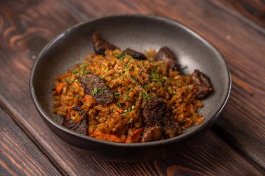 Ahşap arka planda siyah tabakta eti olan geleneksel pilav, menü için fotoğraf