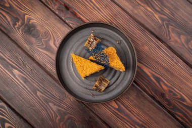 Süslü, siyah güzel bir tabakta, ahşap arka planda ballı pasta.