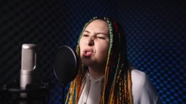 Renkli saçlı kız bir kayıt stüdyosunda ateşli bir şarkı söylüyor.