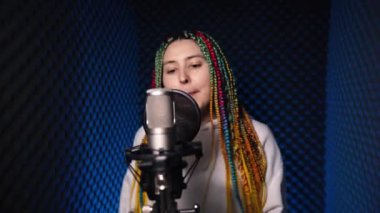 Kafasında örgülü saçları olan neşeli bir kız şarkısını kaydediyor.