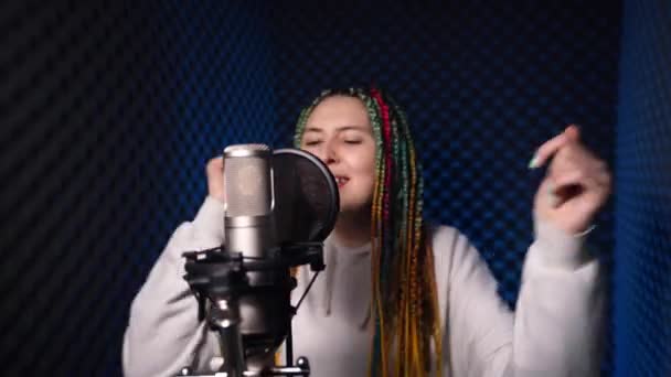 Uma menina alegre, com tranças coloridas na cabeça, está gravando sua música — Vídeo de Stock