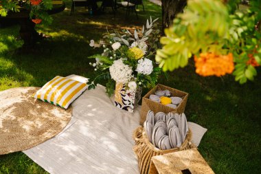 Yeşil çimenlikte yaz pikniği alanı, çiçek aranjmanı, örgü bir halı ve tek kullanımlık terliklerle dolu bir kutu ve bir battaniye.