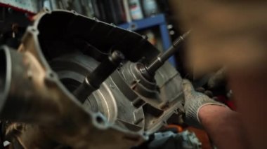 İş eldivenli bir adam ATV şanzımanının cıvatalarını sıkıyor.