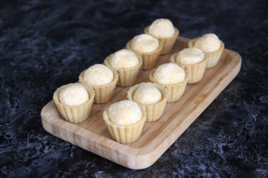 Ahşap dikdörtgen bir plaka ve siyah bir arkaplan dolduran küçük tartlar.