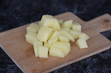 Küçük tahta bir tahtanın üzerinde küçük küplere kesilmiş taze patatesler.