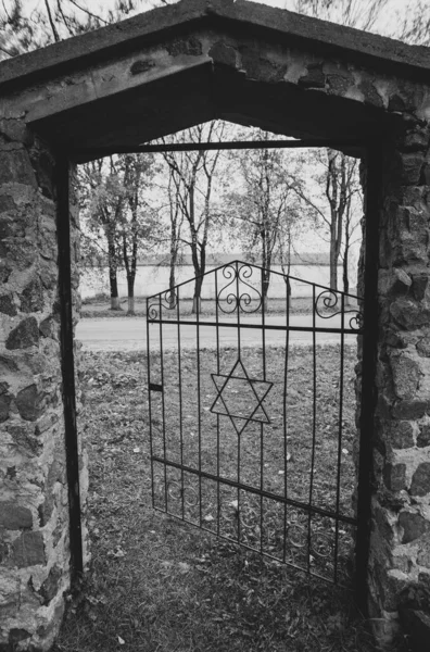 Old ancient historical Jewish cemetery open door gate with a Star of David. A black and white photo with dark gloomy atmosphere.