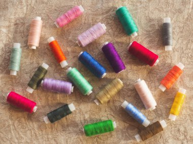 Kahverengi kırsal keten kumaş üzerindeki parlak turuncu, kırmızı, mavi, yeşil iplikçiklerin çeşitliliği. Dikiş ya da el yapımı mağazalar web sitesi ya da sosyal ağ sayfası tasarımı ya da reklamları için bir kalıp arkaplanı