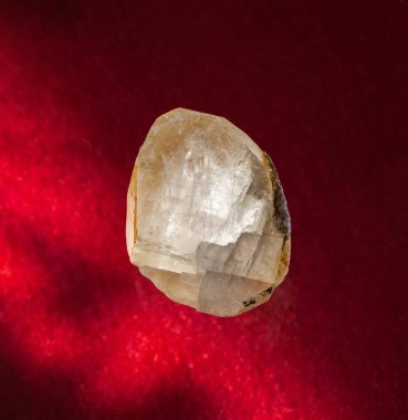 Rusya, Ural 'dan şeffaf kalsit mineral kristali. Kırmızı arkaplanda bir taşın arka plan fotoğrafı. Jeoloji web siteleri, taş koleksiyonu kataloğu, Doğal Bilim Müzesi duvar çizelgesi