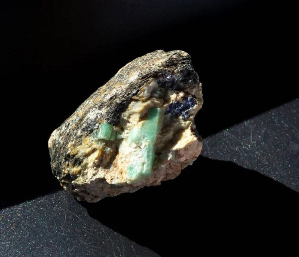 Ακατέργαστοι κρύσταλλοι πολύτιμων λίθων μέσα σε feldspar βράχο με μολυβδαινίτη, μαρμαρυγία και απατίτη εγκλείσματα σε μαύρο φόντο. Από την Ουράλια Ρωσία. — Φωτογραφία Αρχείου