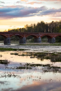 Akşam üzeri Venta nehri üzerindeki tarihi tuğla köprünün manzarası. Fotoğraf Letonya 'da çekildi.