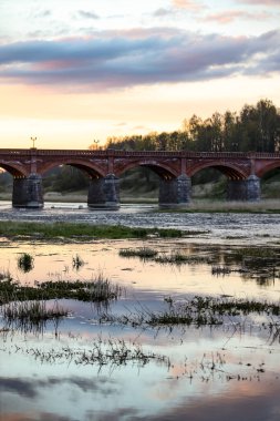 Akşam üzeri Venta nehri üzerindeki tarihi tuğla köprünün manzarası. Fotoğraf Letonya 'da çekildi.