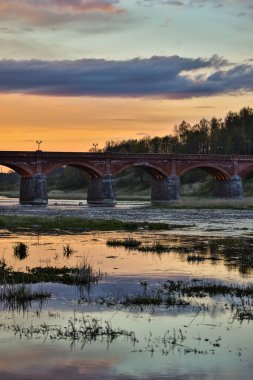 Akşam üzeri Venta nehri üzerindeki tarihi tuğla köprünün manzarası. Fotoğraf Letonya 'da çekildi.