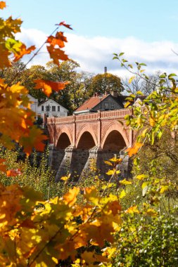 Venta nehri üzerinde eski tuğla köprüsü olan güneşli bir manzara. Fotoğraf, sıcak bir sonbahar gününde çekildi, sarı yapraklar. Fotoğraf Avrupa 'da çekildi.
