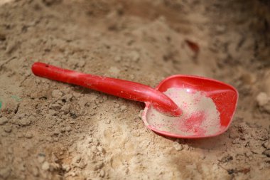 Çocukların oyun parkı için küçük kırmızı plastik kum küreği. Fotoğraf sıcak bir yaz gününde çekildi..