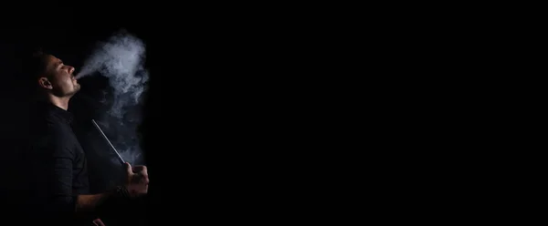 Geleneksel nargile piposu içen bir adamla yatay afiş. Adam siyah arka planda fotokopi aletiyle duman üflüyor. Hookh Bar için sigara konsepti. Metin için yer