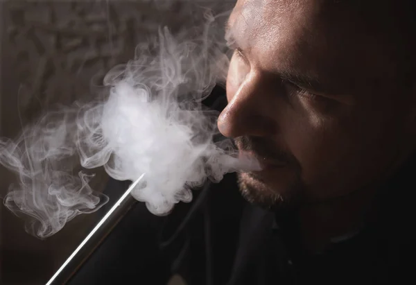 男人在黑暗的背景下从呼救烟斗里喷出烟雾 特写吸烟的男人在Hookah休息厅 吸烟概念 — 图库照片